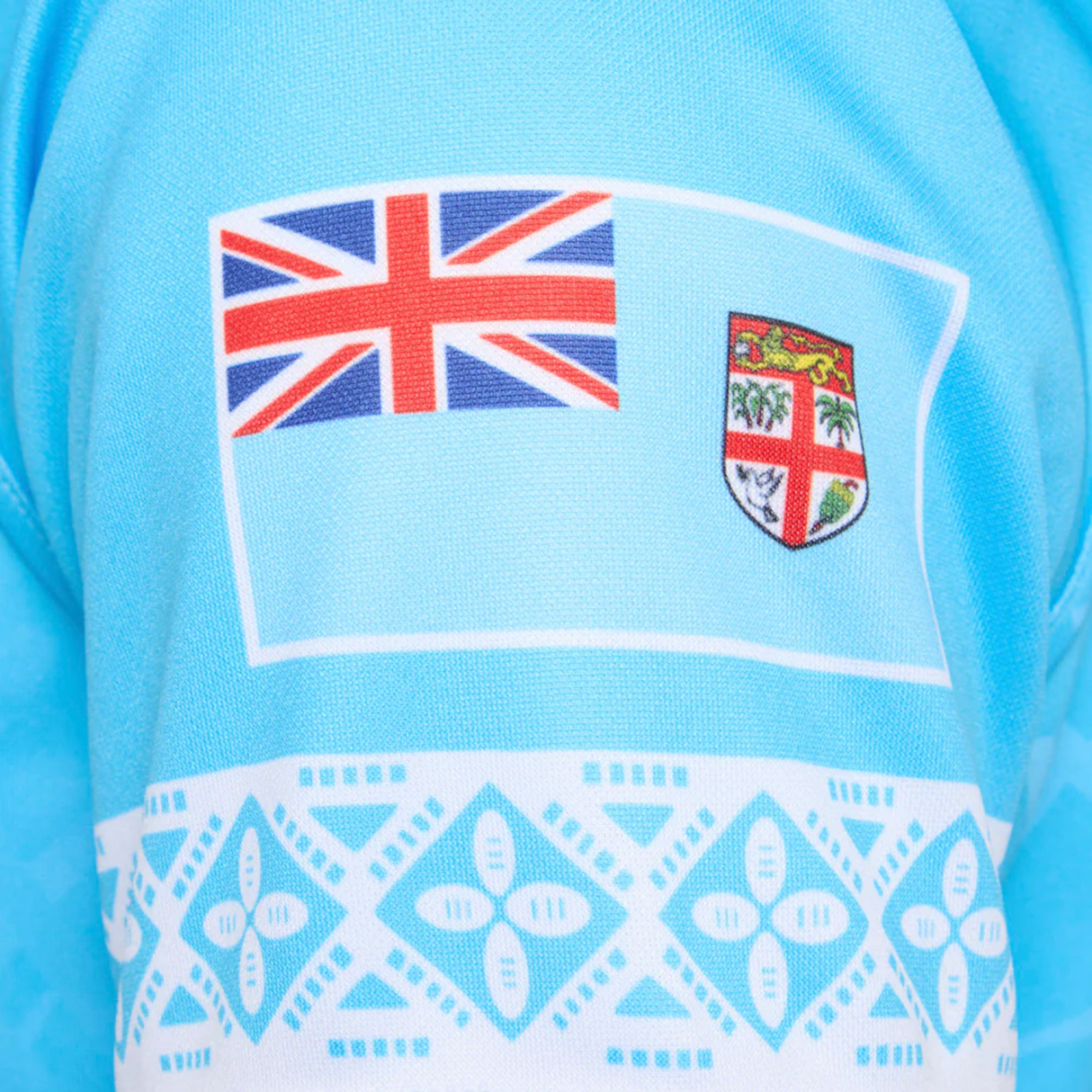 Close-up of the Fiji 25/26 Replica Away Jersey by Umbro, an athletic fit blue polyester rugby top with the national flag and white geometric masi art patterns, inspired by traditional Fijian design.