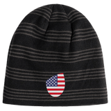 The EMB Canterbury USA Shield Beanie sports a dark striped pattern with an American flag shield emblem prominently on the front.
