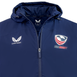 The USA Rugby Long Length Bench Jacket by Castore is a navy blue jacket featuring the Castore logo on the left side and the USA Rugby logo on the right. It includes a front zipper and a hood, making it ideal for staying warm while showing team support.