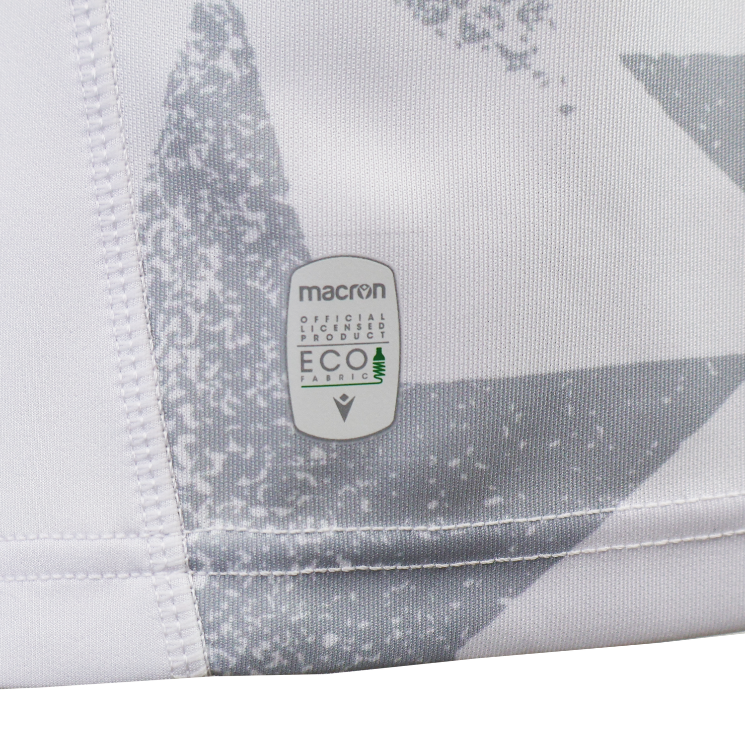 Close-up of the USA Rugby WRWC25 Replica Away Jersey by Macron, featuring a "Macron Official Licensed Product ECO Fabric" label stitched onto its white and gray patterned fabric.