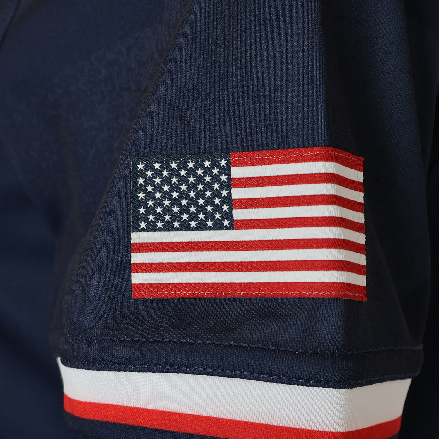 A close-up of an American flag patch on the sleeve of the Women's USA Rugby WRWC25 Replica Home Jersey by Macron, featuring a white and red striped cuff—ideal for showing support at the Women's Rugby World Cup 2025.