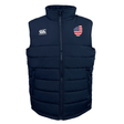 The USA Shield Core Gilet by EMB Canterbury is a navy blue puffer vest with an American flag patch on the left chest, a company logo on the right chest, Thermoreg insulation, and a front zipper.