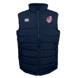 The USA Shield Core Gilet by EMB Canterbury is a navy blue puffer vest with an American flag patch on the left chest, a company logo on the right chest, Thermoreg insulation, and a front zipper.