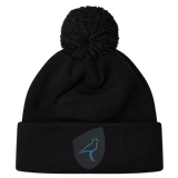 The Uruguay Shield Pom Pom Beanie by EMB Canterbury showcases a stylish black design with a striking blue bird logo on the front, combining fashion and warmth perfectly.