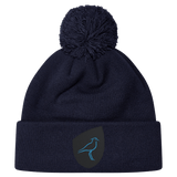 The Uruguay Shield Pom Pom Beanie by EMB Canterbury is dark blue with a playful pom-pom on top, adorned with a small patch showcasing a blue bird logo.