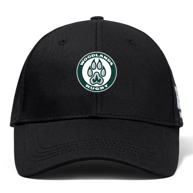 The Woodlands Youth Flexfit Drill Cap by Canterbury is a black cap from EMB Canterbury, featuring the embroidered Woodlands Rugby logo with a paw print inside a green and white circle on the front.