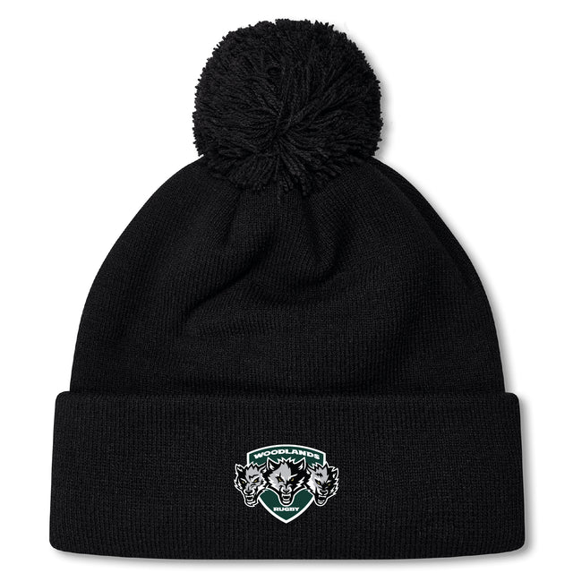 The Woodlands Youth Wolfpack Pom Pom Beanie by Canterbury from EMB Canterbury is a black knit, fleece-lined beanie with a large pom-pom and a "Woodlands Rugby" logo patch with three wolves on the folded brim.