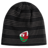 The Wales Shield Beanie by EMB Canterbury is a black and gray striped beanie showcasing a fierce red dragon emblem on a classic white and green shield.