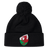 The EMB Canterbury Wales Shield Pom Pom Beanie is a stylish black beanie with a striking patch featuring a red dragon against a green and white backdrop, reminiscent of the Wales Shield.