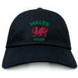 The EMB S&S Activewear Nations of Rugby Wales Dad Cap is a black cap with "WALES RUGBY" and a bold red Welsh dragon emblem on the front—perfect for rugby fans.