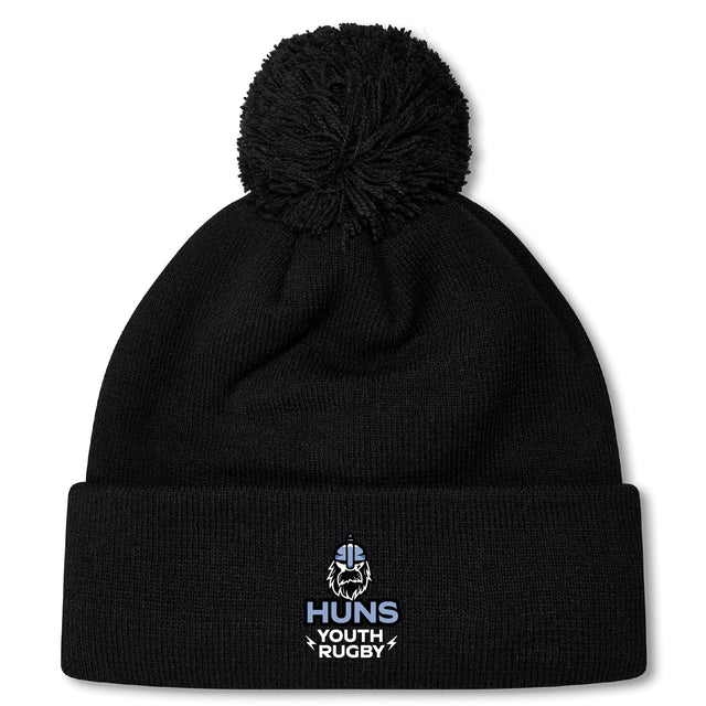Stay warm in the Austin Huns Youth Rugby Pom Pom Beanie by EMB Canterbury, featuring a black knit design, fleece lining, and an embroidered "Huns Youth Rugby" Viking helmet logo on the front.