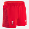 The Wales 25/26 Matchday Home Shorts by Macron are red men's rugby shorts with the Welsh Rugby Union logo on the front left leg, a patterned side panel, and an elastic waistband.