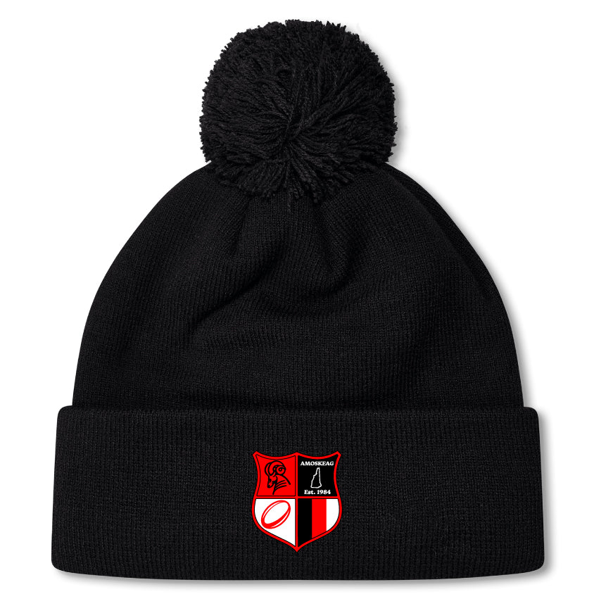 The Amoskeag Rugby Club Pom Pom Beanie by EMB Canterbury features a black design with a red and black embroidered shield patch. Its fleece-lined interior offers warmth on chilly days.