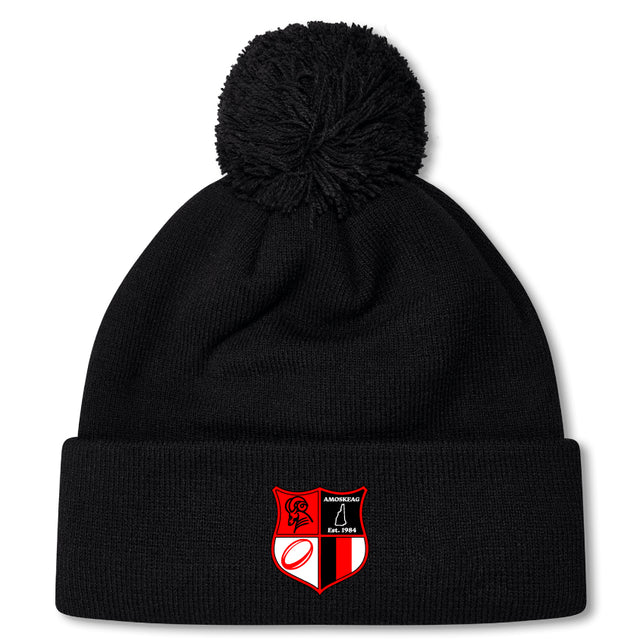 The Amoskeag Rugby Club Pom Pom Beanie by EMB Canterbury features a black design with a red and black embroidered shield patch. Its fleece-lined interior offers warmth on chilly days.