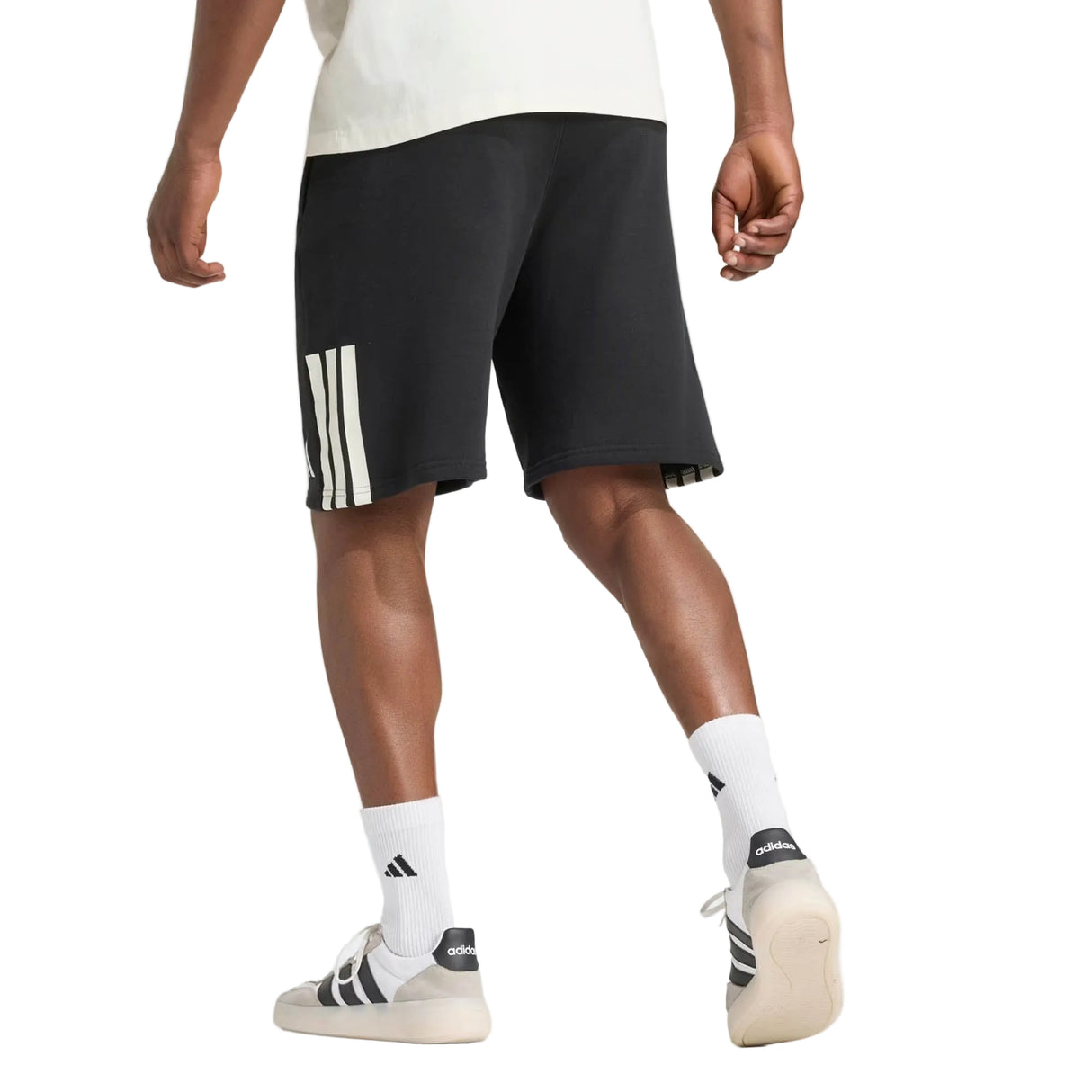 A person is photographed from behind against a plain background, wearing adidas All Blacks 26/27 Leisurewear Shorts with white stripes, paired with white adidas socks and white adidas sneakers.