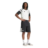 A person stands with one hand on their hip, dressed in black and white adidas sportswear featuring the All Blacks 26/27 Leisurewear Shorts by adidas, paired with matching adidas shoes and socks, against a plain white background.