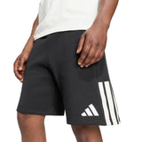 Person wearing adidas All Blacks 26/27 Leisurewear Shorts, featuring black fabric with signature white stripes and adidas branding, standing with hands relaxed by their sides. Only the lower torso and upper legs are visible.