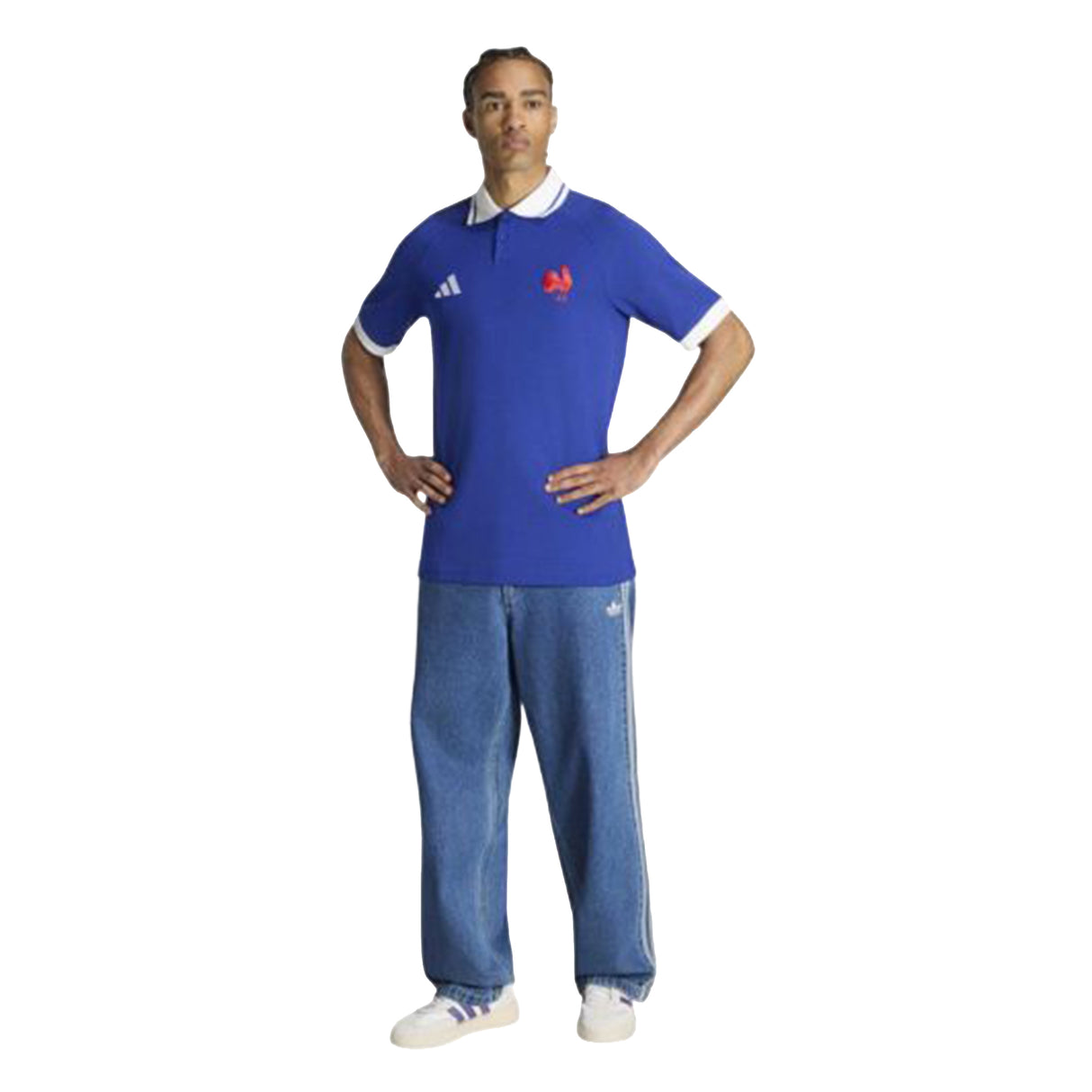 A man stands with hands on hips, wearing the adidas France FFR 26/27 Travel Polo—featuring a white collar—paired with loose blue jeans and white sneakers against a white background.