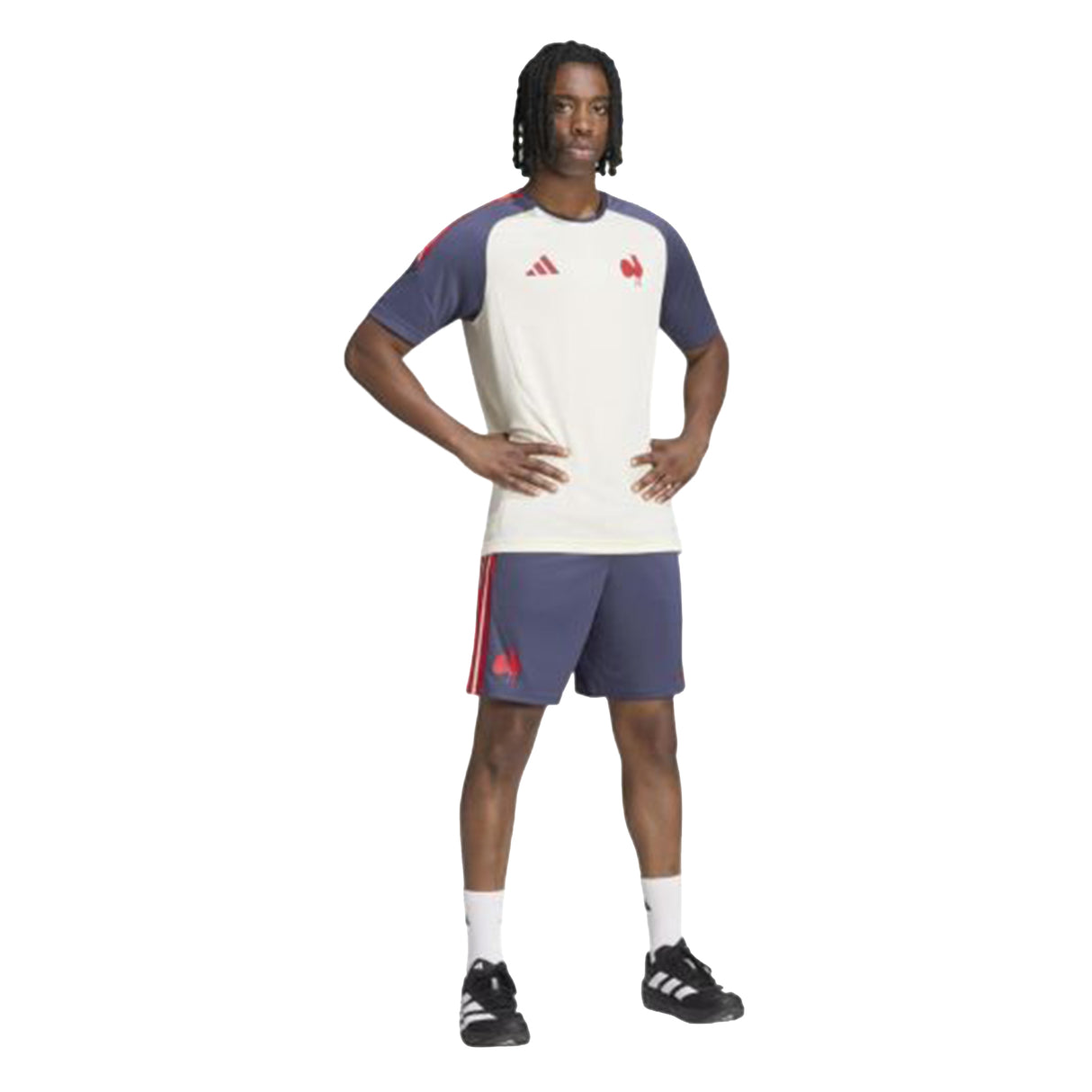 A person stands with hands on hips, wearing the France FFR 26/27 Performance T-Shirt by adidas in off-white and navy, paired with navy shorts featuring red stripes, white socks, and black athletic shoes—a classic look inspired by the French national rugby team.