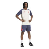 A person stands with hands on hips, wearing the France FFR 26/27 Performance T-Shirt by adidas in off-white and navy, paired with navy shorts featuring red stripes, white socks, and black athletic shoes—a classic look inspired by the French national rugby team.