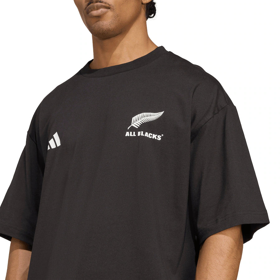 A person wearing the All Blacks 25/26 Presentation T-Shirt by adidas, featuring the adidas logo and silver fern emblem on the chest.