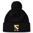 The Conestoga Rugby Pom Pom Beanie by EMB Canterbury is a black knit hat with a pom-pom, fleece lining, and features a gold and white "Conestoga Rugby Club" logo with "EST. 1971" on the front cuff.
