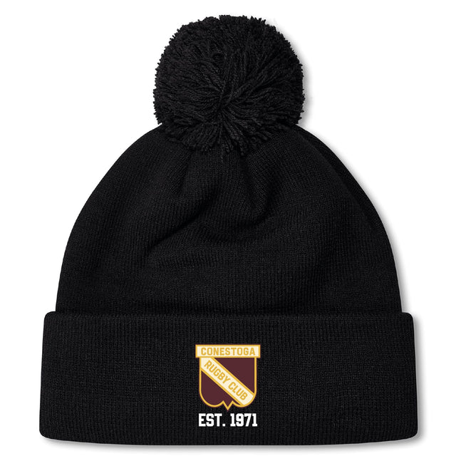 The Conestoga Rugby Pom Pom Beanie by EMB Canterbury is a black knit hat with a pom-pom, fleece lining, and features a gold and white "Conestoga Rugby Club" logo with "EST. 1971" on the front cuff.