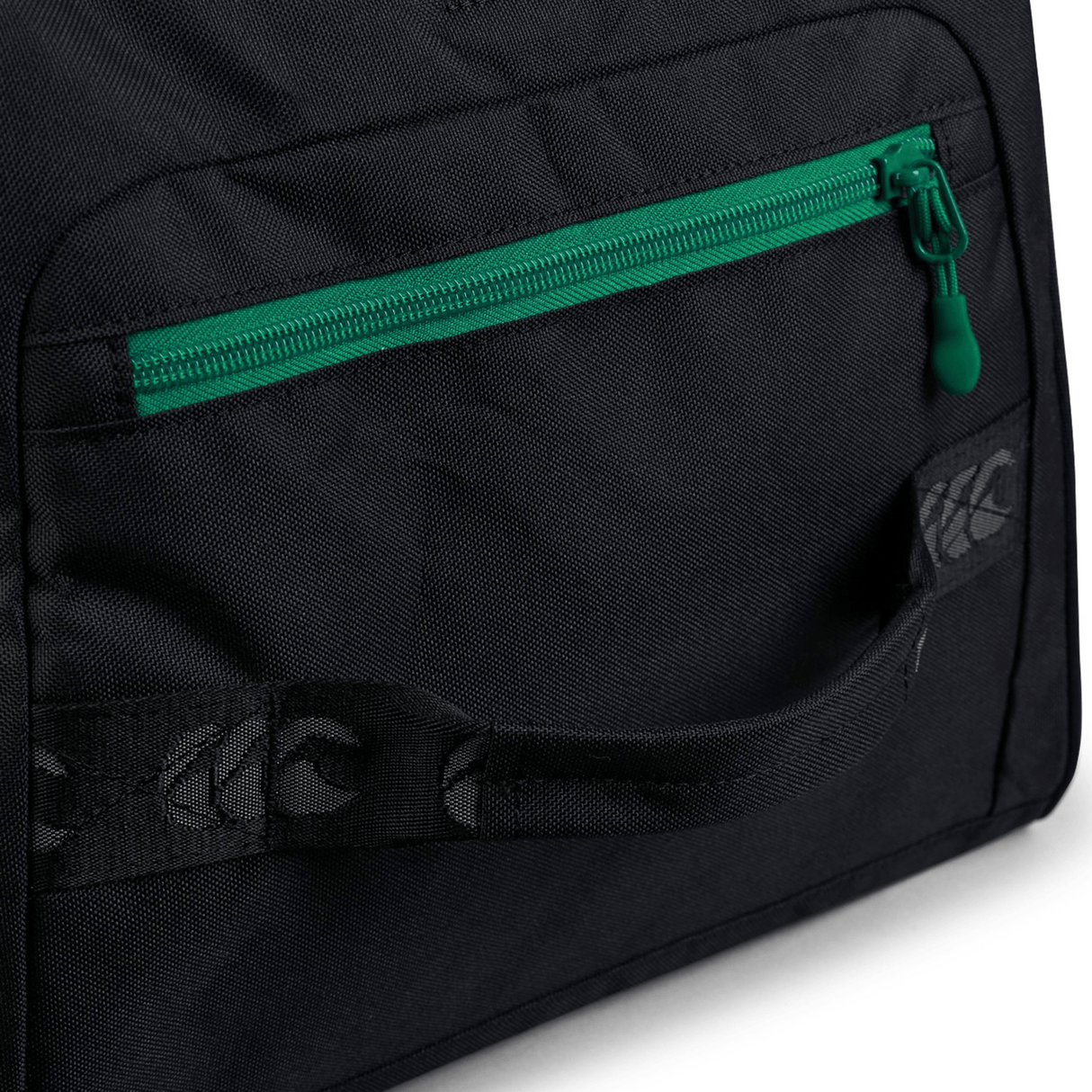 Close-up of the Ireland 24 Holdall Duffle Bag by Canterbury showcasing a black fabric with a green-zippered front pocket, a strap handle, and a subtle circular pattern near the handle.