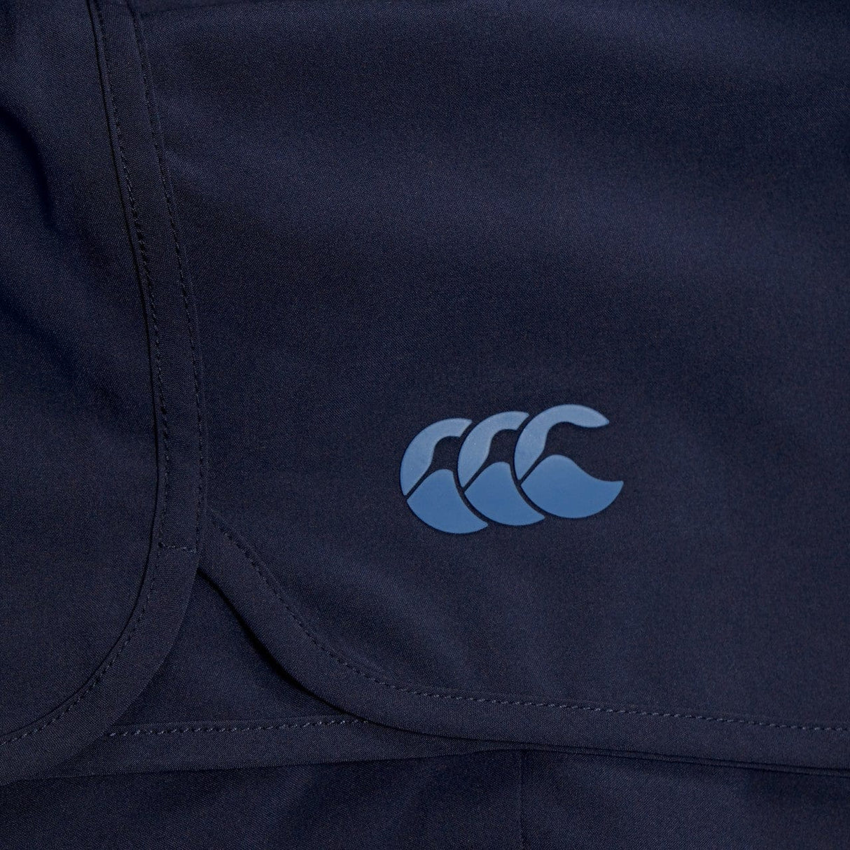 Close-up of a dark blue Canterbury Elite Woven gym short with a triple crescent moon logo in light blue on the lower right corner.