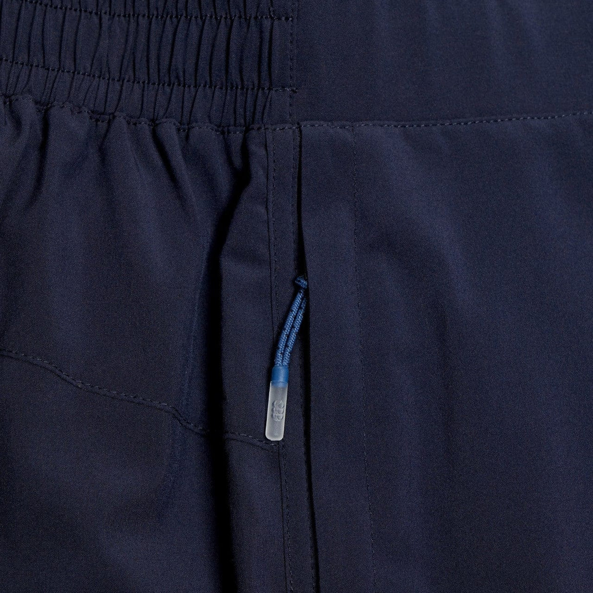 Close-up of a dark navy Canterbury Elite Woven Short fabric with a detailed view of zippered pockets and a blue zipper pull.