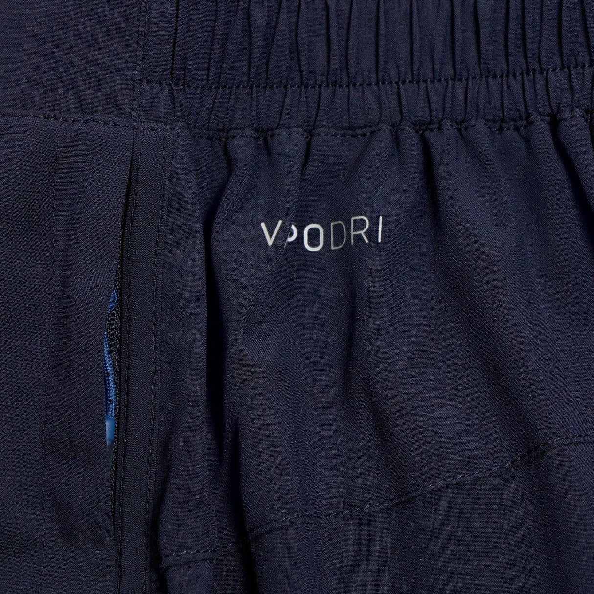 Close-up of dark blue Canterbury Elite Woven gym short fabric with a white "vuori" logo and a small blue zippered pocket.