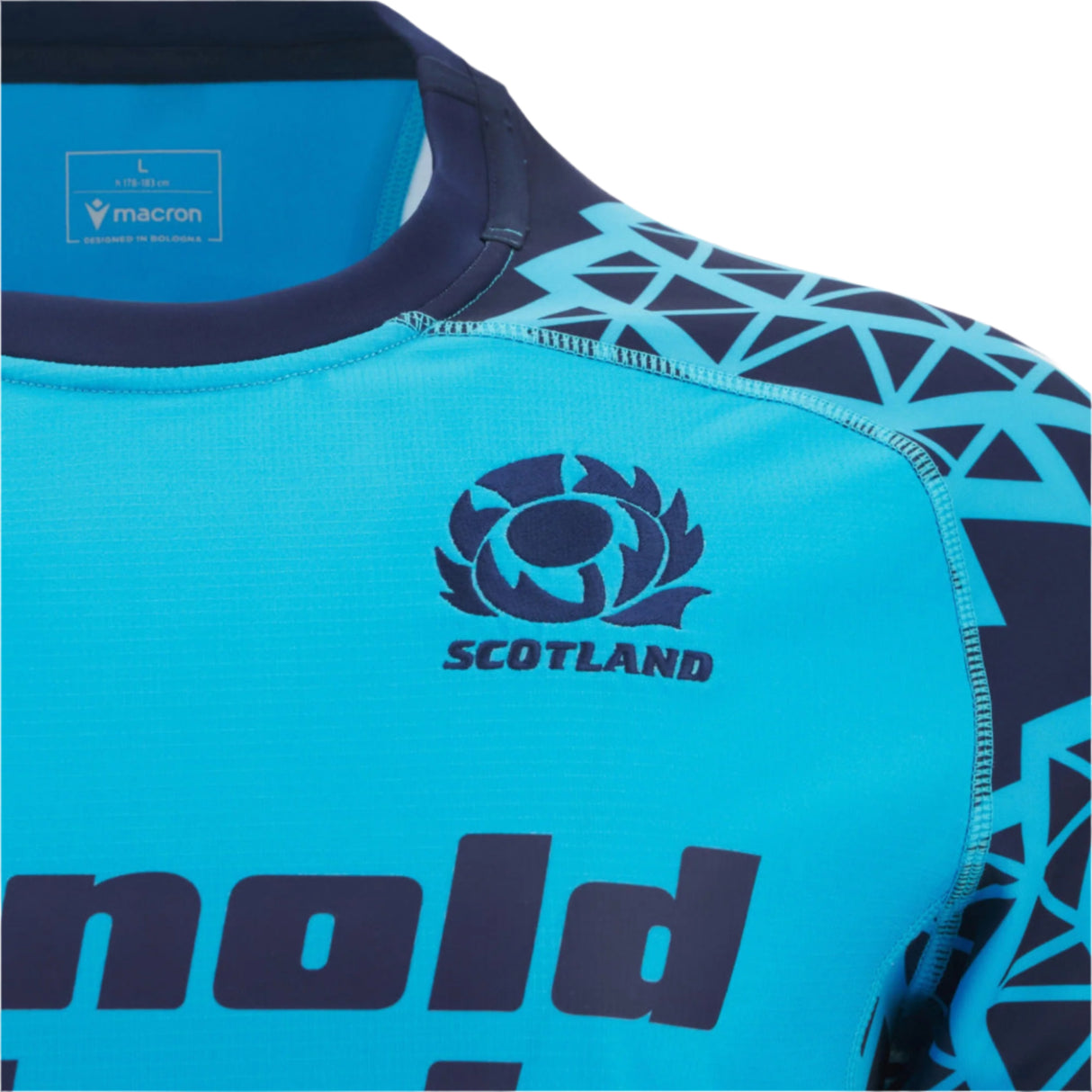 Close-up of the Scotland 25/26 Sky Training Jersey by Macron, featuring geometric patterns, the Scottish Rugby logo on the chest, and a Macron brand label inside the collar.
