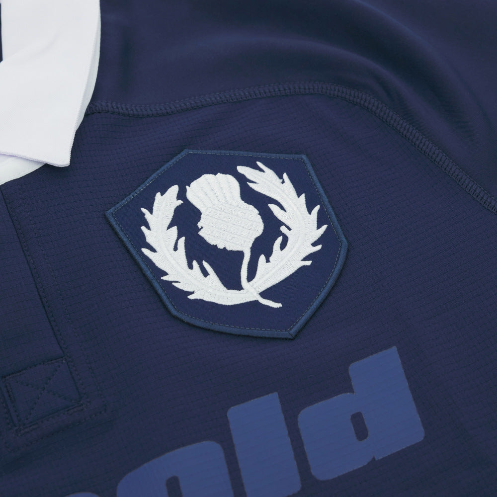 Close-up of the Scotland Rugby Union 1925 100th Anniversary Authentic Home Jersey by Macron in navy, showing a white thistle emblem inside a shield, part of a white collar, and partially visible text below.