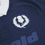 Close-up of the Scotland Rugby Union 1925 100th Anniversary Authentic Home Jersey by Macron in navy, showing a white thistle emblem inside a shield, part of a white collar, and partially visible text below.
