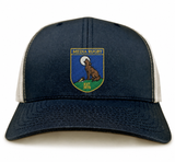 The Media Rugby Retro Trucker Cap by EMB S&S Activewear is a navy and white hat featuring a “Media Rugby” patch with a howling wolf, “Est 1973” text, and an adjustable snapback closure.