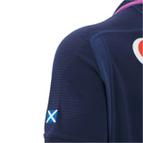 Close-up of a person wearing the Women's Scotland 25/26 Replica Home Jersey by Macron, featuring a navy blue design and a small Scottish flag patch on the sleeve.