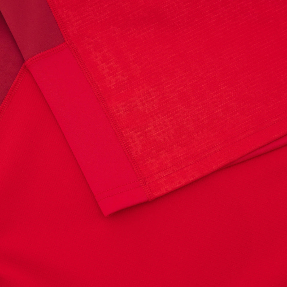 Close-up of overlapping red fabrics with varied textures, echoing the geometric patterns seen on the Wales 25/26 Authentic Matchday Home Jersey by Macron.
