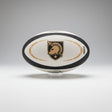 The Army West Point Gilbert Omega Match Ball by Gilbert displays a black and gold logo with helmet, sword, and star, set on a clear stand against a gray background.