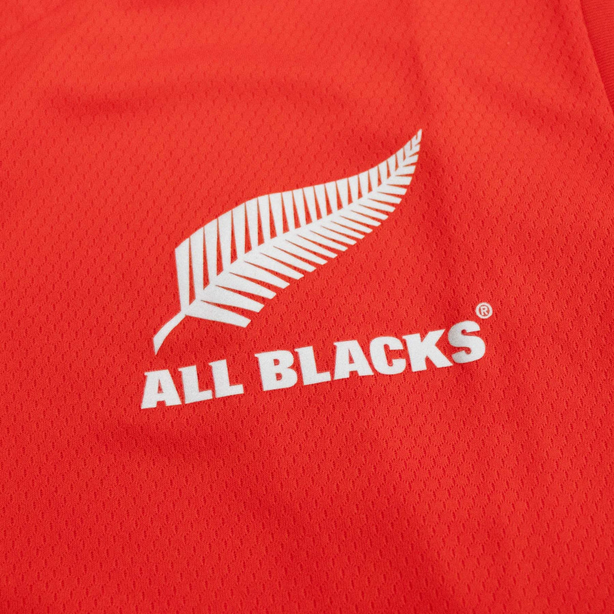 A close up of the All Blacks Red Singlet by adidas logo on a red shirt.