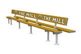 A long yellow aluminum Custom Shelter bench with "the mill" and a spartan helmet logo printed on its backrest, supported by metal legs on a white background.