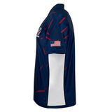 The USA Rugby 23/24 Home Jersey by Castore features navy blue with red streaks, white side panels, a chest logo, and an American flag patch on the sleeve—a perfect replica for Eagles fans, shown from the left side.
