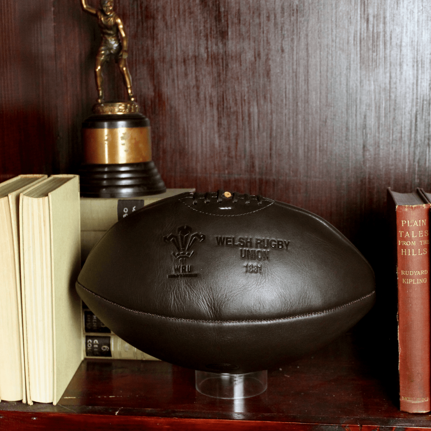 A Wales Rugby Vintage Leather Ball by Gilbert on a shelf next to books.