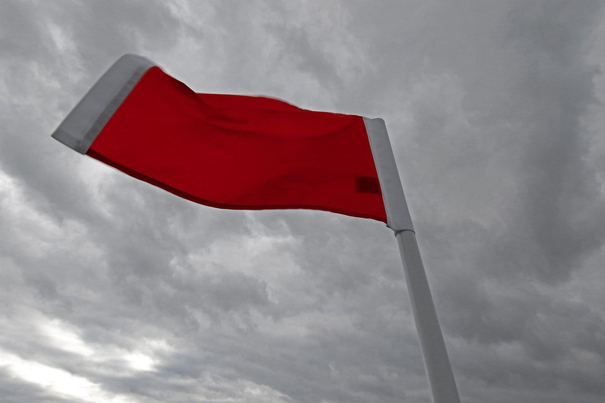 A red Kwik Goal Premier Corner Flag fluttering against a cloudy sky, attached to a white pole on the left side.